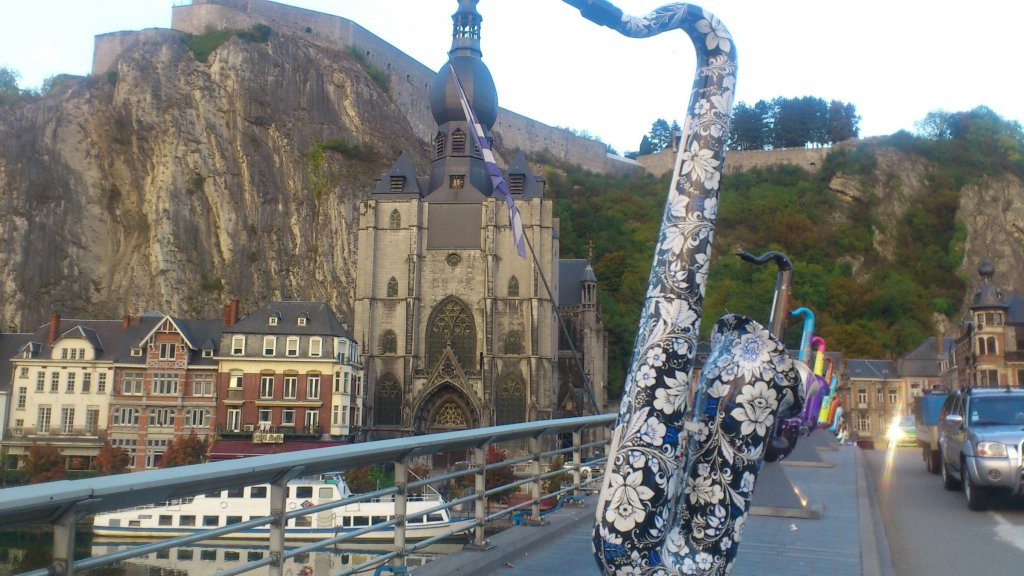 A view of a bridge featuring colorful saxophone sculptures, with a historic church and rocky cliffs in the background.