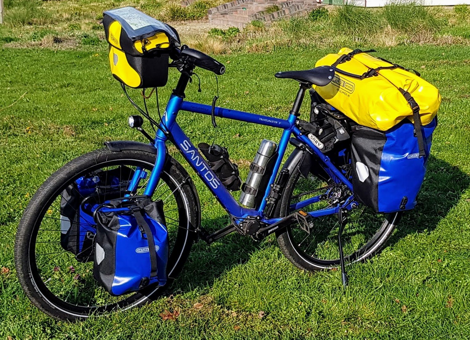 Materiaal voor je fietsvakantie Blue touring bicycle loaded with yellow and blue pannier bags on green grass