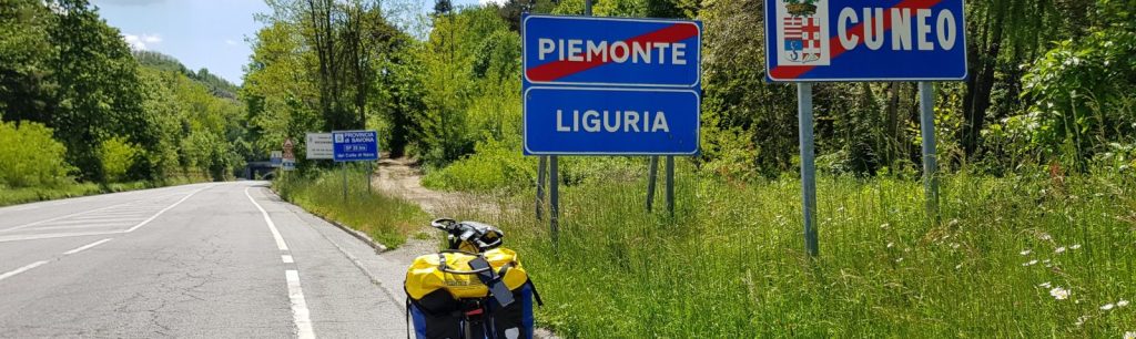 Road sign indicating the borders of Piemonte, Liguria, and Cuneo, with a bicycle in the foreground