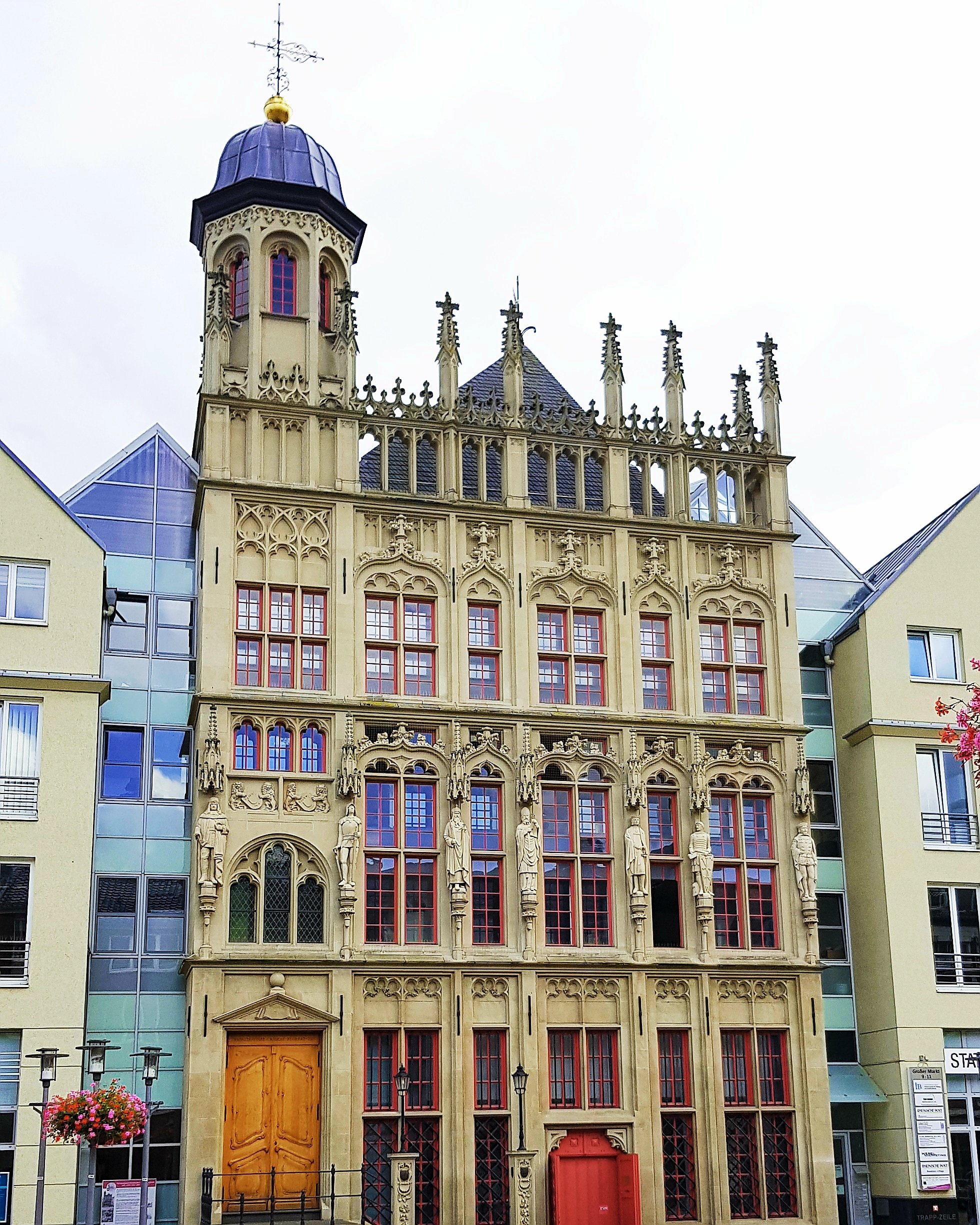 Historic building with Gothic architecture featuring ornate details, statues, and a distinctive tower, set against modern buildings.