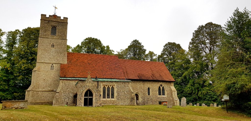 A historic stone church with a tall tower and a rustic red roof, surrounded by trees and a graveyard.