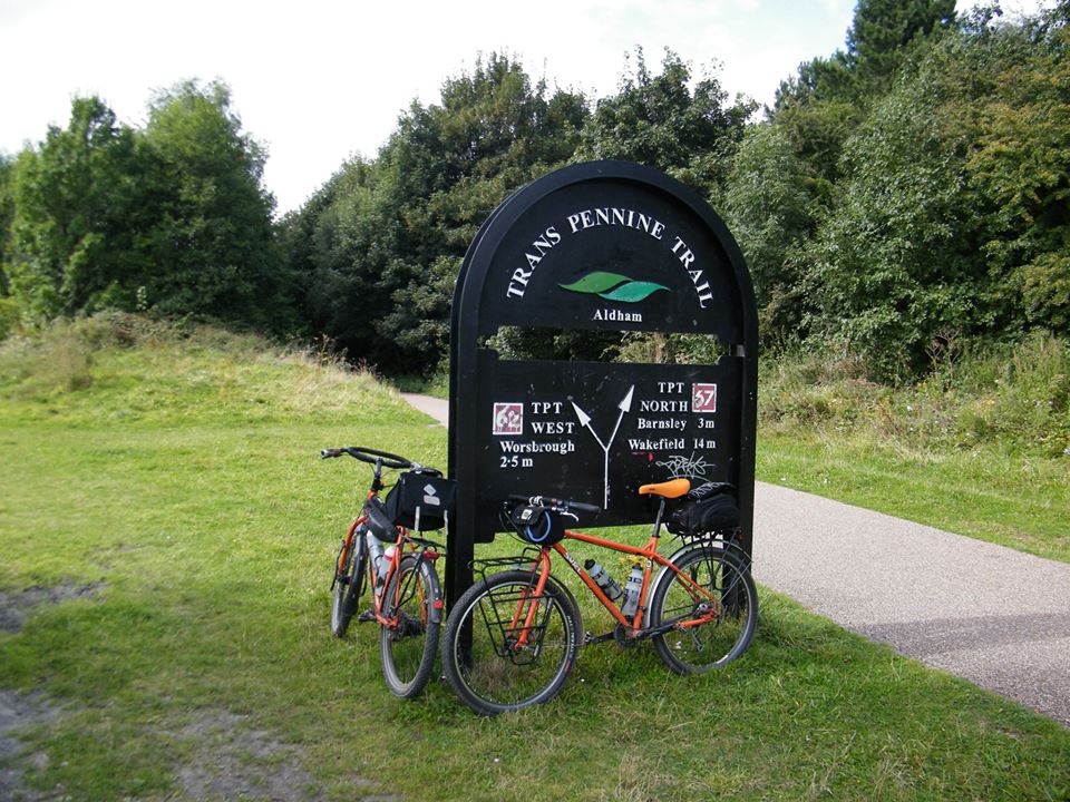 Two bicycles parked at the Trans Pennine Trail sign in Aldham, with directional information and distances to nearby locations.