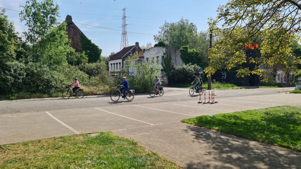 Fietsers rijden door een groene omgeving met vervallen gebouwen op de achtergrond.