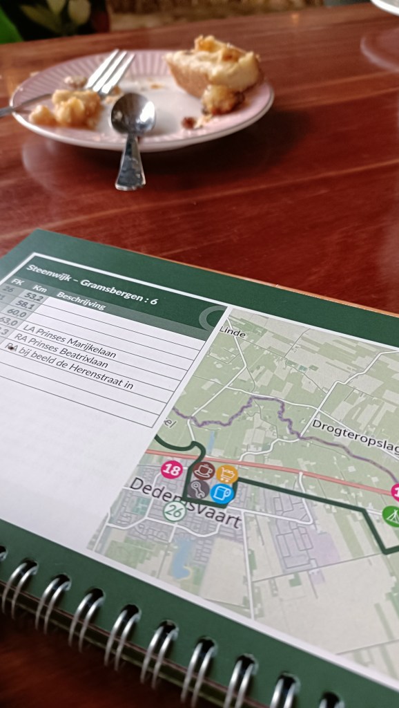 Een plattegrond van Dedemsvaart met informatie over een fietstocht, naast een leeg bord en een vork op een tafel.