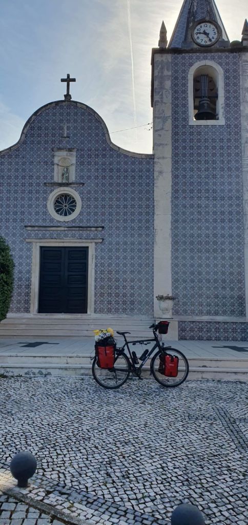 Fiets met rode zadeltassen voor een kerk met decoratieve tegels en een klok in Portugal.