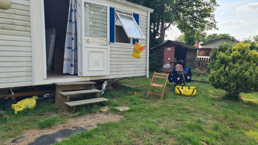 Camping accommodation with a small porch, steps leading up, and a bicycle parked nearby, surrounded by green grass.