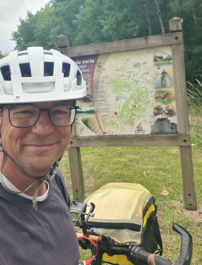 Een man met een fietshelm staat naast een fiets, met een kaart van de omgeving op de achtergrond.