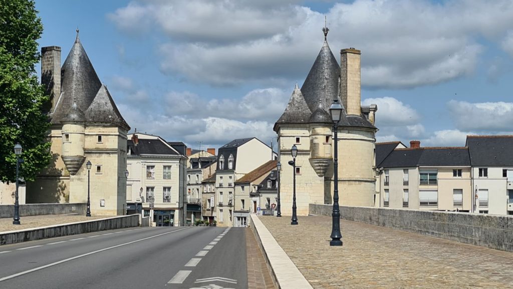 Een straatzicht met middeleeuwse torens en gebouwen onder een blauwe lucht met enkele wolken.