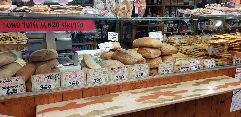 Brood voor je fietsvakantie onderweg. Een bakkerij met verschillende soorten brood, inclusief integro, pugliese, en altamura, met prijzen zichtbaar op het toonbank.