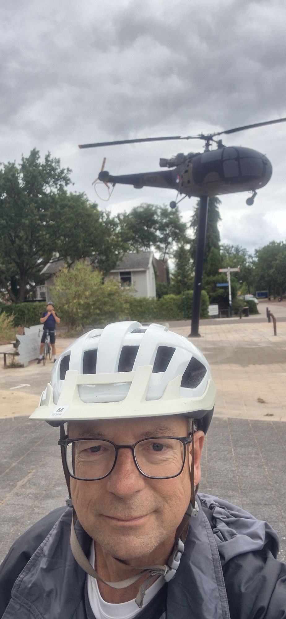 Cyclist wearing a white helmet poses beneath a helicopter sculpture in a park
