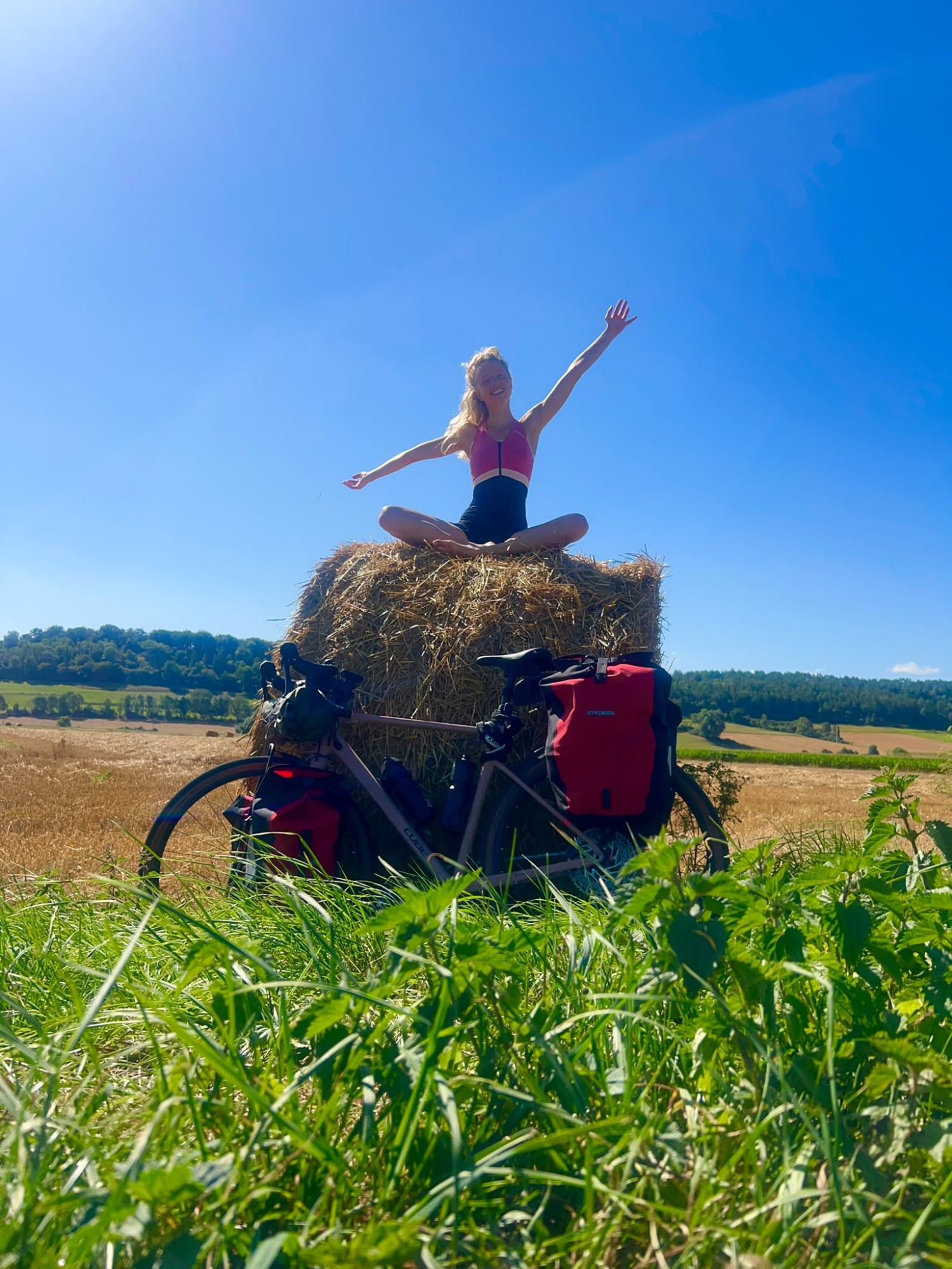Woman practicing yoga on a hay bale beside touring bicycles in a sunny rural field
